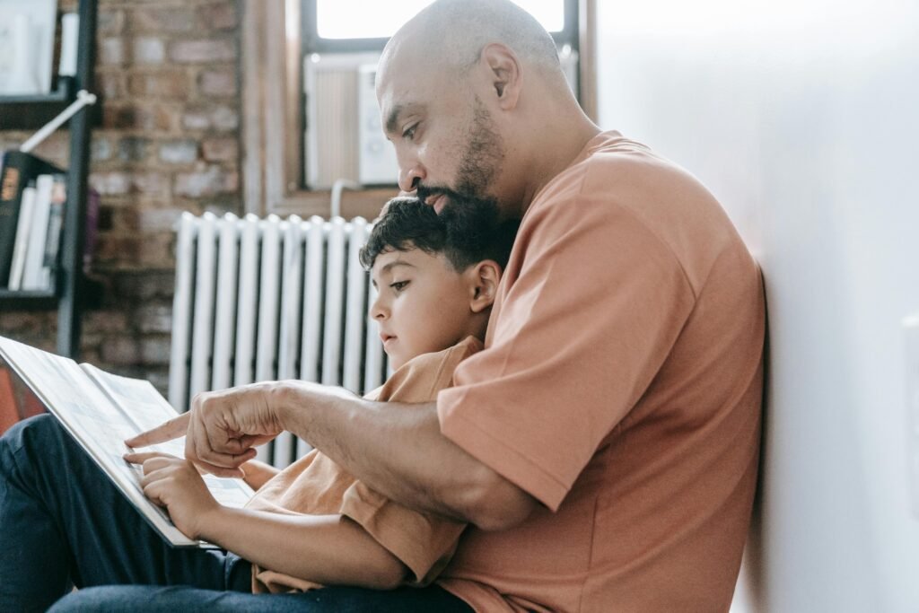 A father teaches his son to read, creating a warm bonding moment in a cozy home setting.